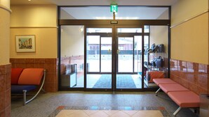 A hotel lobby with a reception desk, a waiting area with chairs, and a view of the outside through the glass doors. - Toyooka Sky Hotel (Toyooka)