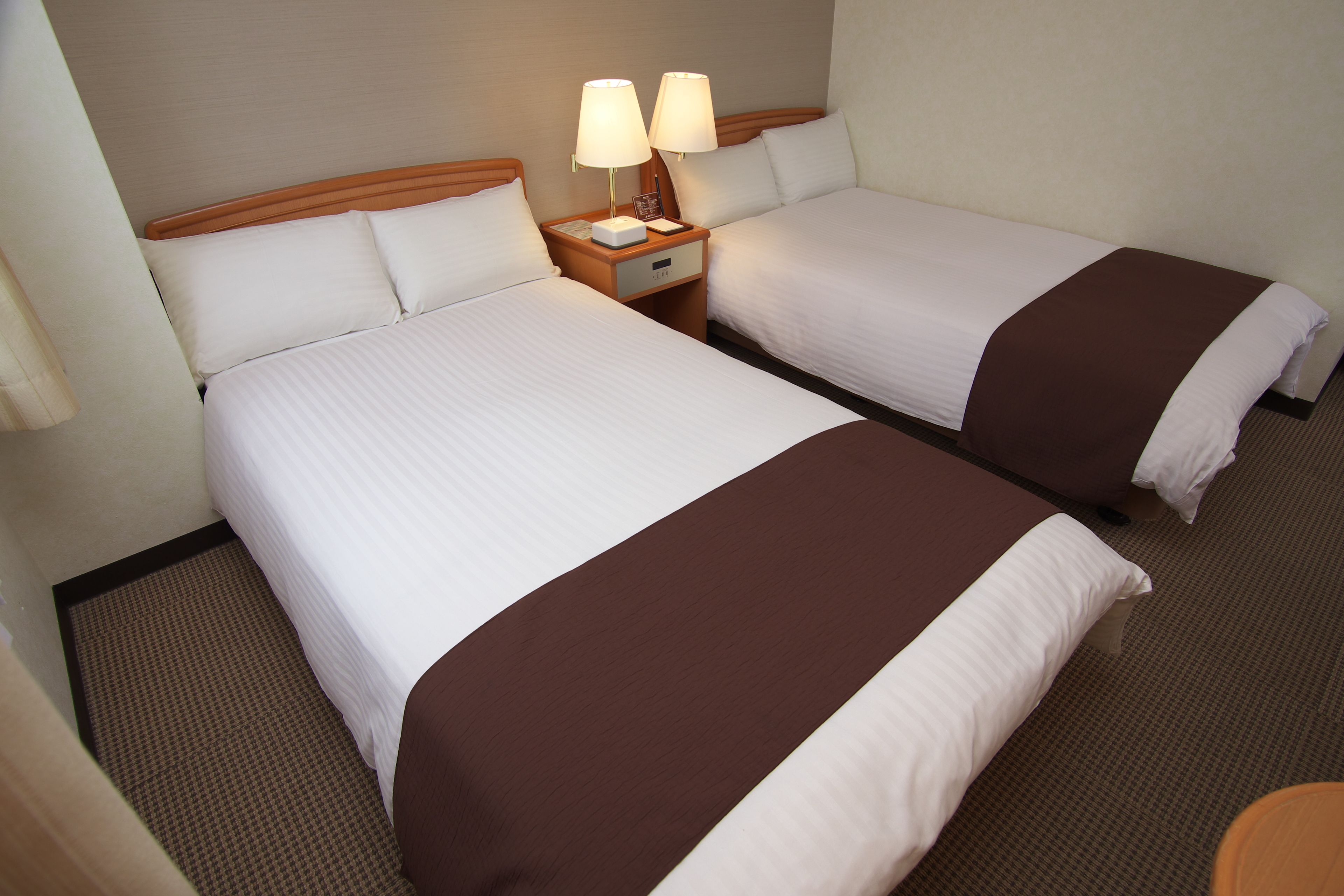 Two adjacent beds with white linens and brown throw blankets, each with a bedside table featuring a lamp and a clock.