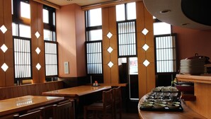 A restaurant with wooden tables and chairs, a counter with stacked plates, and a view through shoji screens. - Toyooka Sky Hotel (Toyooka)
