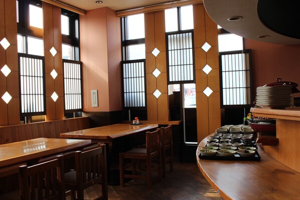 Un restaurant amb taules i caires de fusta, una barra amb plats apilats i una vista a través de pantalles shoji.