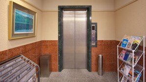 An elevator with a digital display, a magazine rack with brochures, and a framed picture on the wall. - Toyooka Sky Hotel (Toyooka)