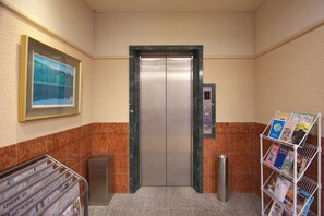 An elevator with a digital display, a magazine rack with brochures, and a framed picture on the wall. - Toyooka Sky Hotel (Toyooka)