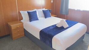 Ein Hotelzimmer mit einem großen Bett, einem Nachttisch aus Holz, einer Schublade und einem Fenster mit Vorhängen.