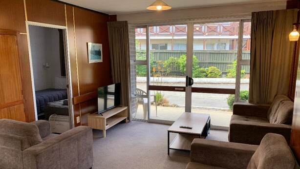 Ein Hotelzimmer mit einer Sofagarnitur, einem Fernseher, einem kleinen Tisch und Blick auf ein Gebäude sowie Grünflächen.