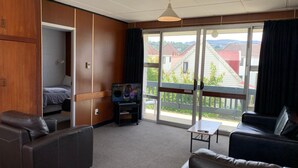 Ein modernes Wohnzimmer mit Sofa, Fernseher und Balkon mit Blick auf Häuser.