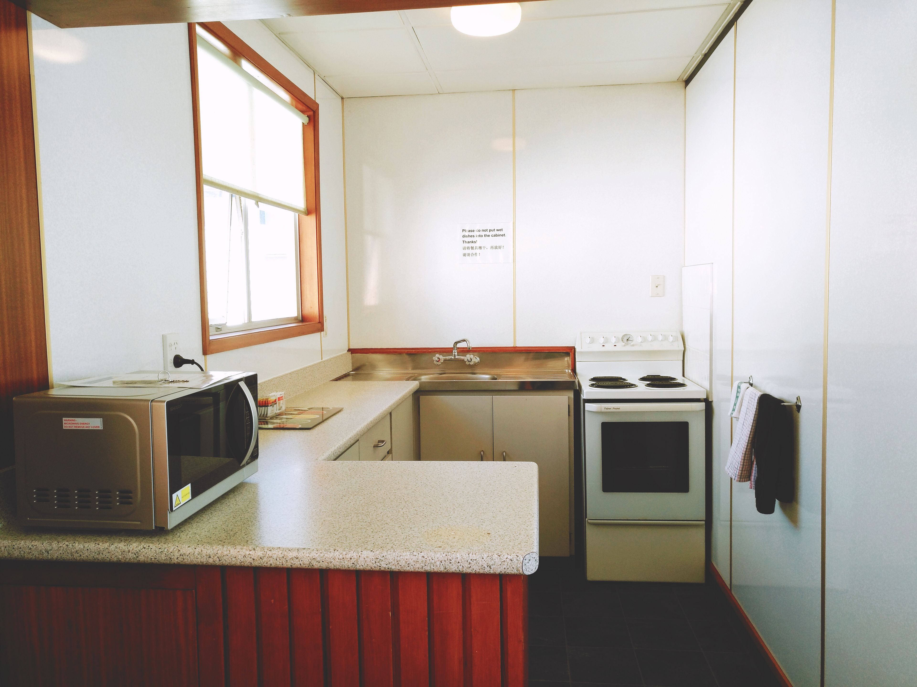 A compact kitchen with a microwave, stove, sink, and a window.