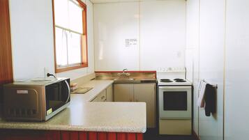 A compact kitchen with a microwave, stove, sink, and a window.