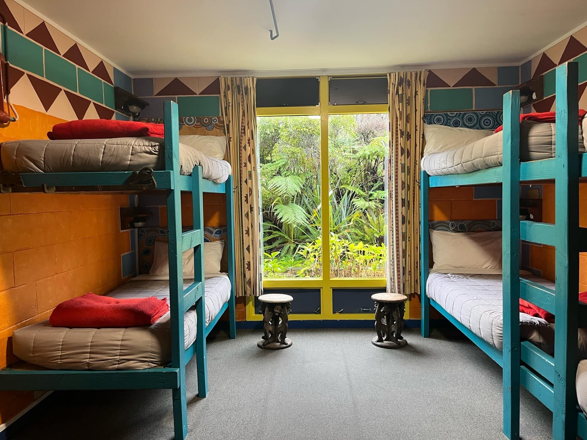 Un dormitorio con literas, una ventana que da a zonas verdes y dos taburetes pequeños.