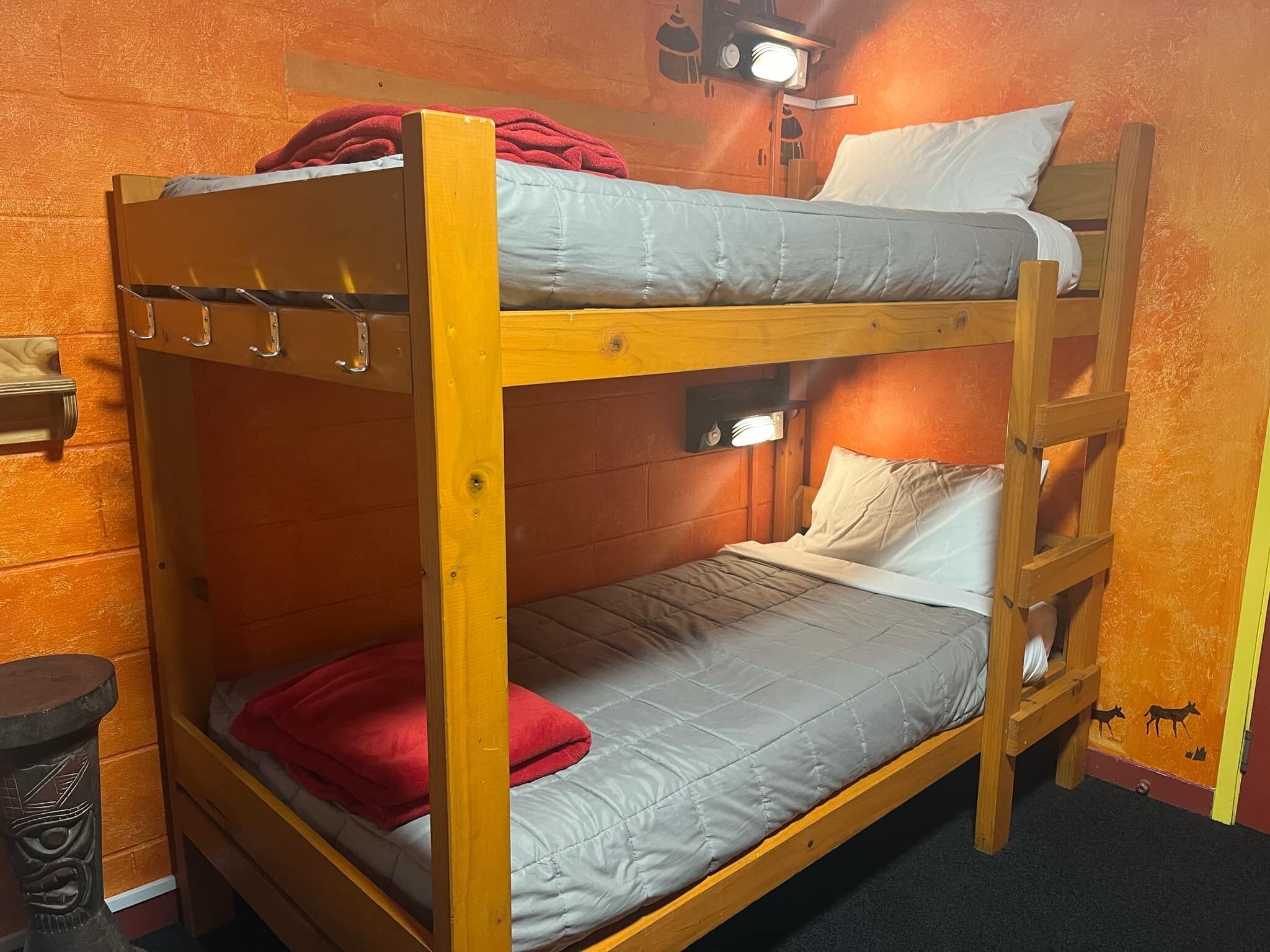 Una cama individual con cabecera, una toalla roja y una mesita con un objeto decorativo.