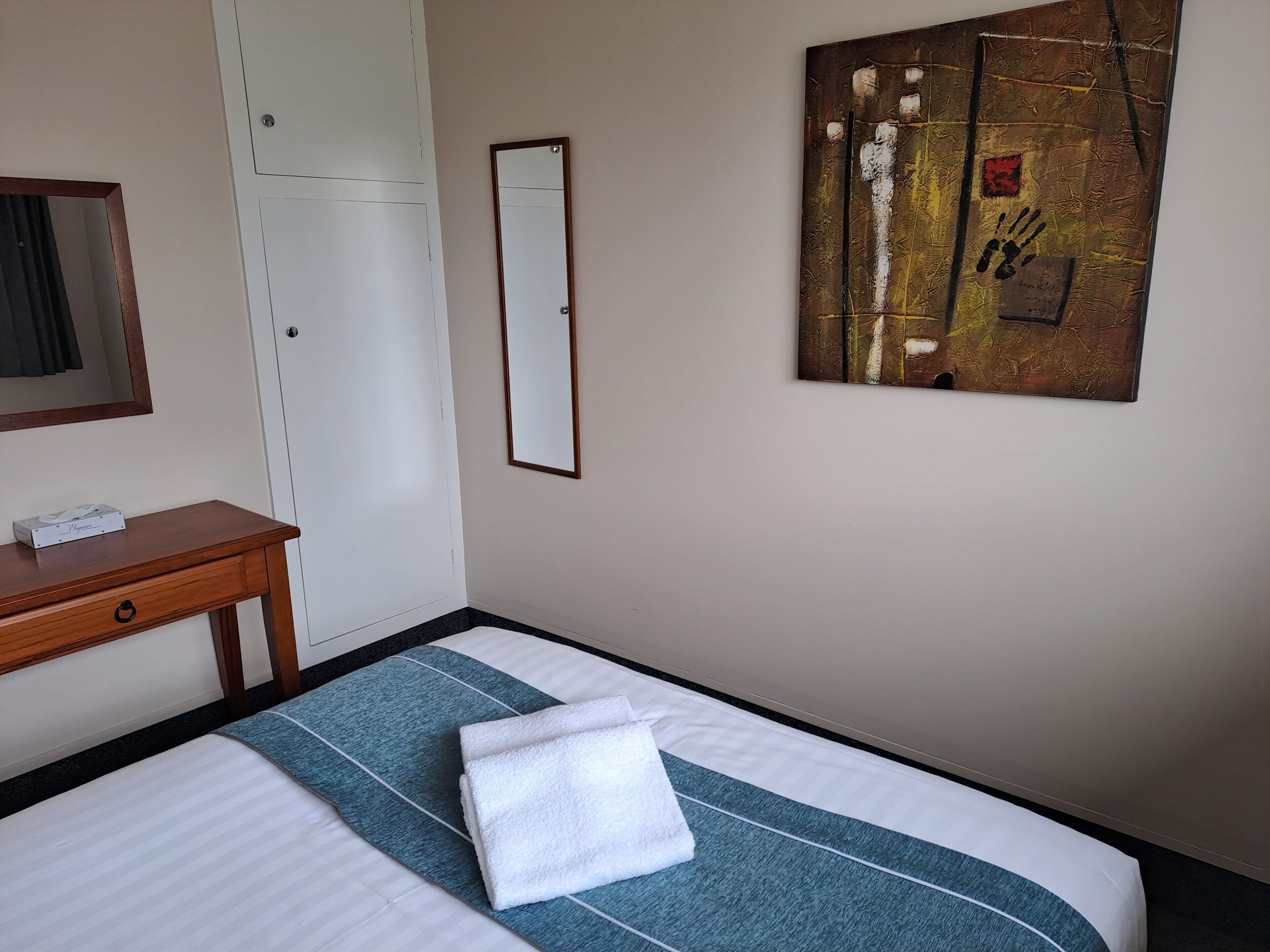 Una habitación de hotel con una cama, un escritorio, un espejo y un cuadro en la pared.
