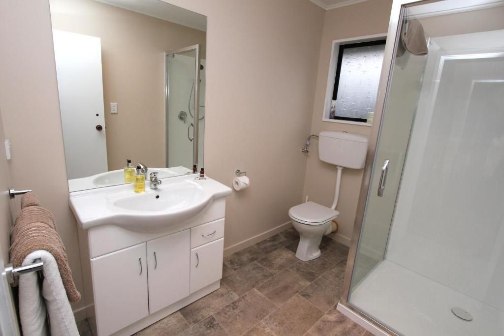 A bathroom with a white sink, mirror, toilet, and glass-enclosed shower.