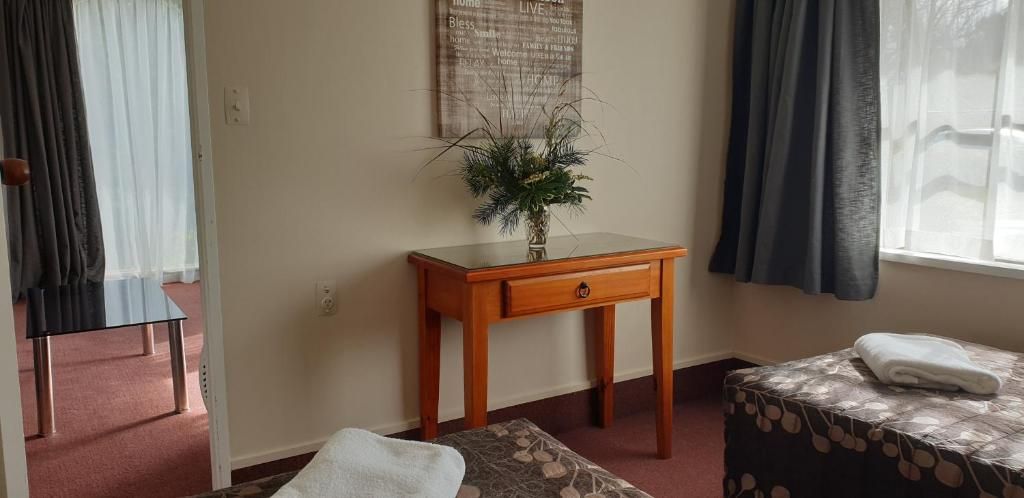 Habitación de hotel con cama, una mesita de madera con un florero, ventana con cortinas y piso alfombrado.