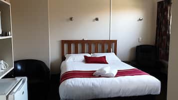 A hotel room with a bed, a desk with a microwave, a chair, and a wardrobe.