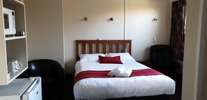 A hotel room with a bed, a desk with a microwave, a chair, and a wardrobe. - Commodore Motor Lodge (Ashburton)