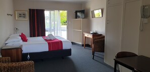 A hotel room with a bed, a desk, a chair, a telephone, and a television. - Commodore Motor Lodge (Ashburton)