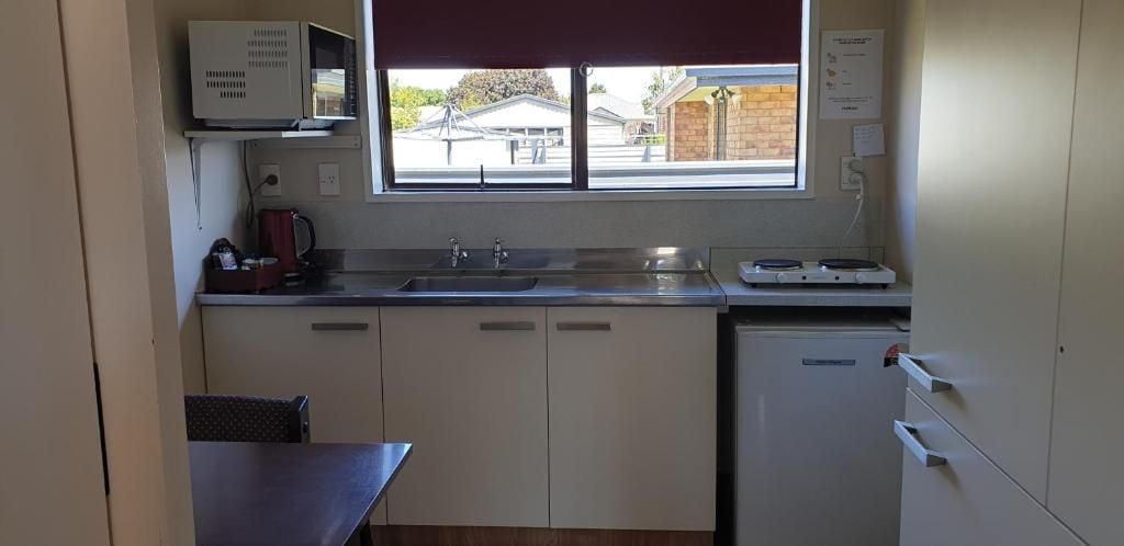 Una cocina compacta con ventana, microondas, lavamanos y un refrigerador pequeño.