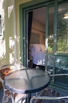 Una habitación con una cama, un vidrio que da a un balcón y una mesa con sillas.