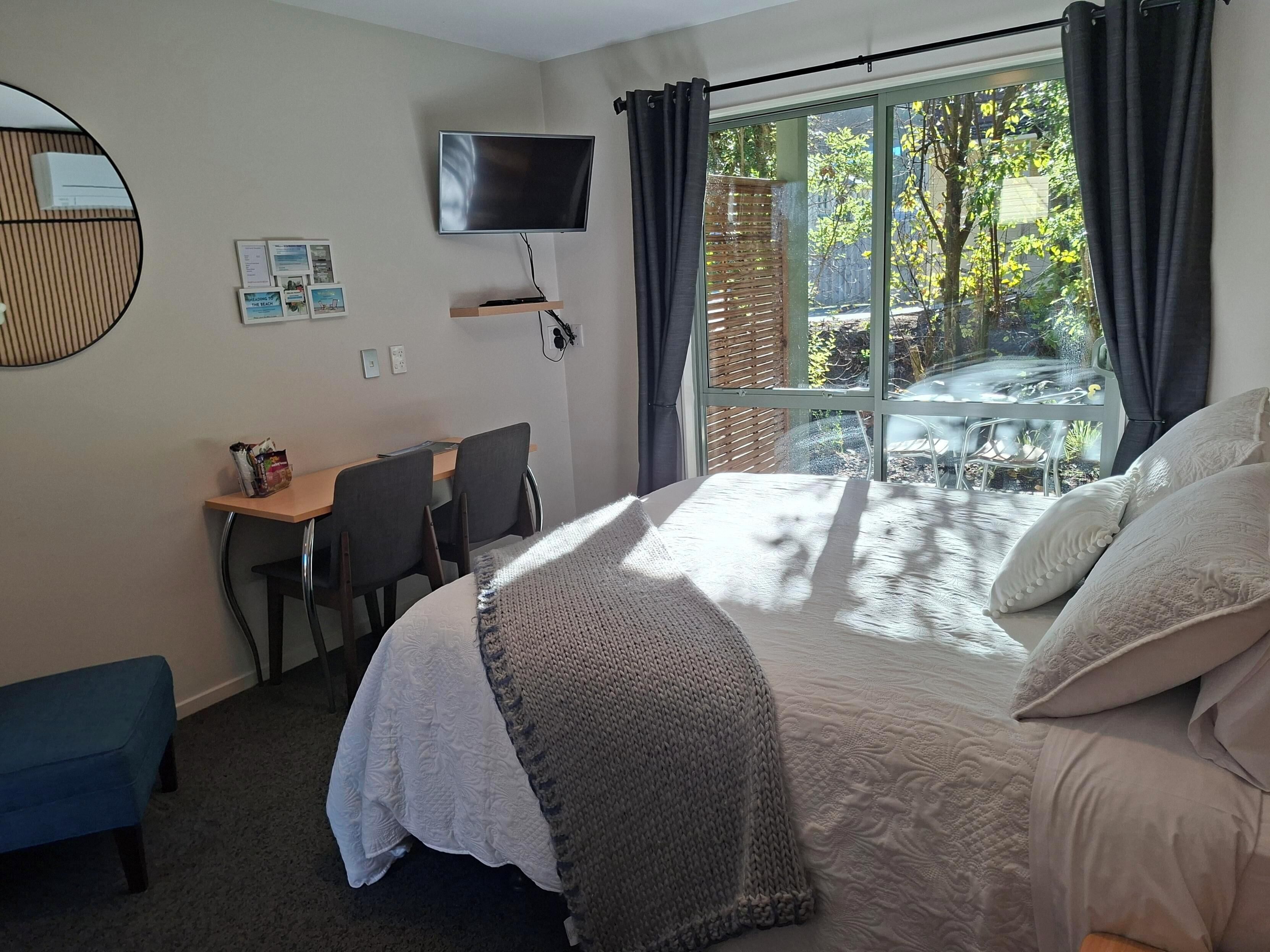 A hotel room with a bed, a desk, a chair, a television, and a window with a view of the outdoors.