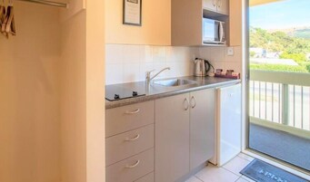 Una cocina con armarios blancos, un lavamanos de acero inoxidable y un microondas.