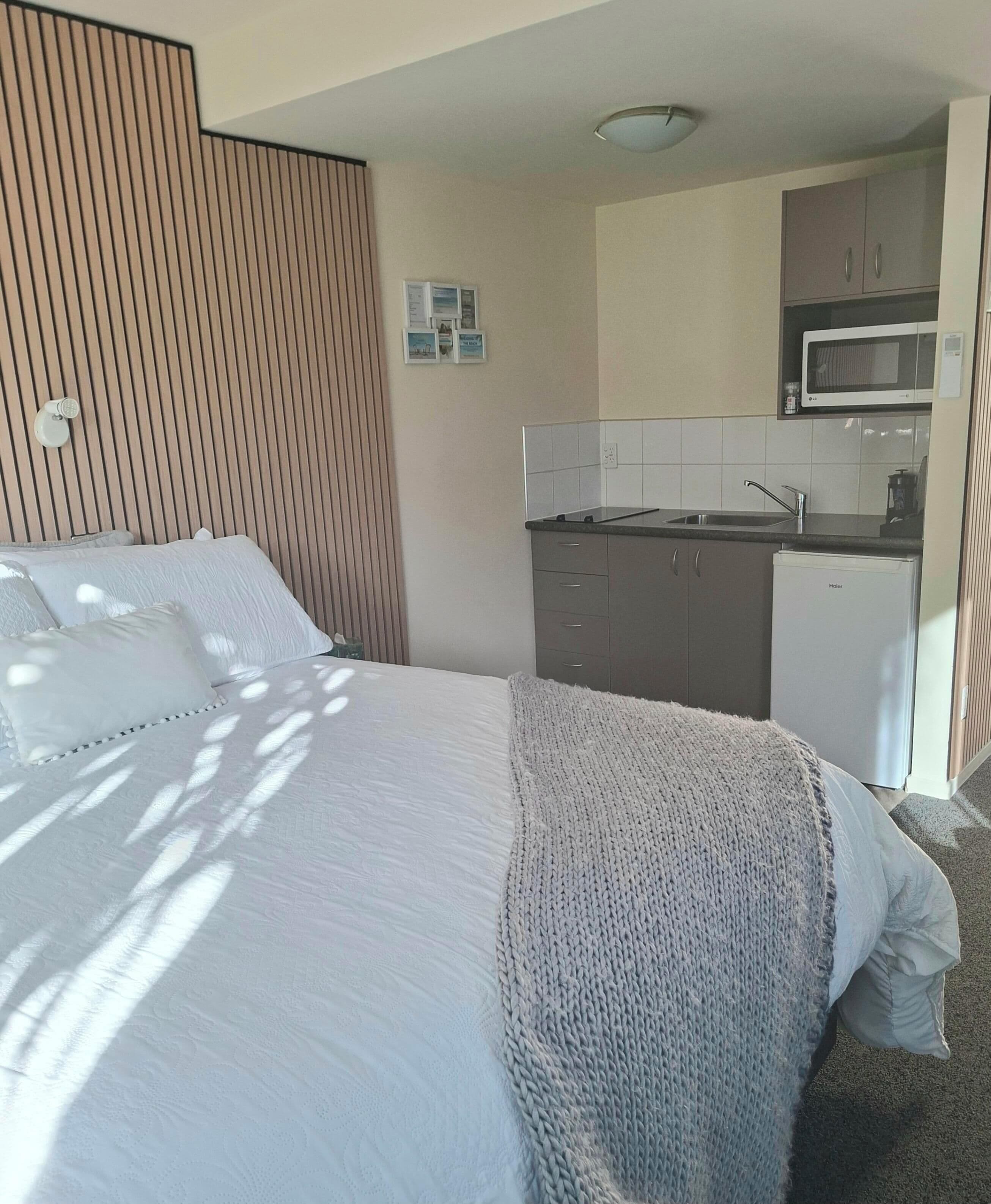 Et hotelværelse med en seng, et tekøkken og en vægmonteret lampe.