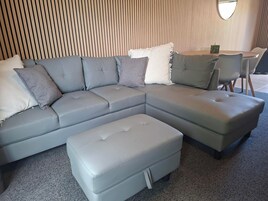 Una sala moderna con un sofá seccional gris, un reposapiés a juego y una mesita con una silla.