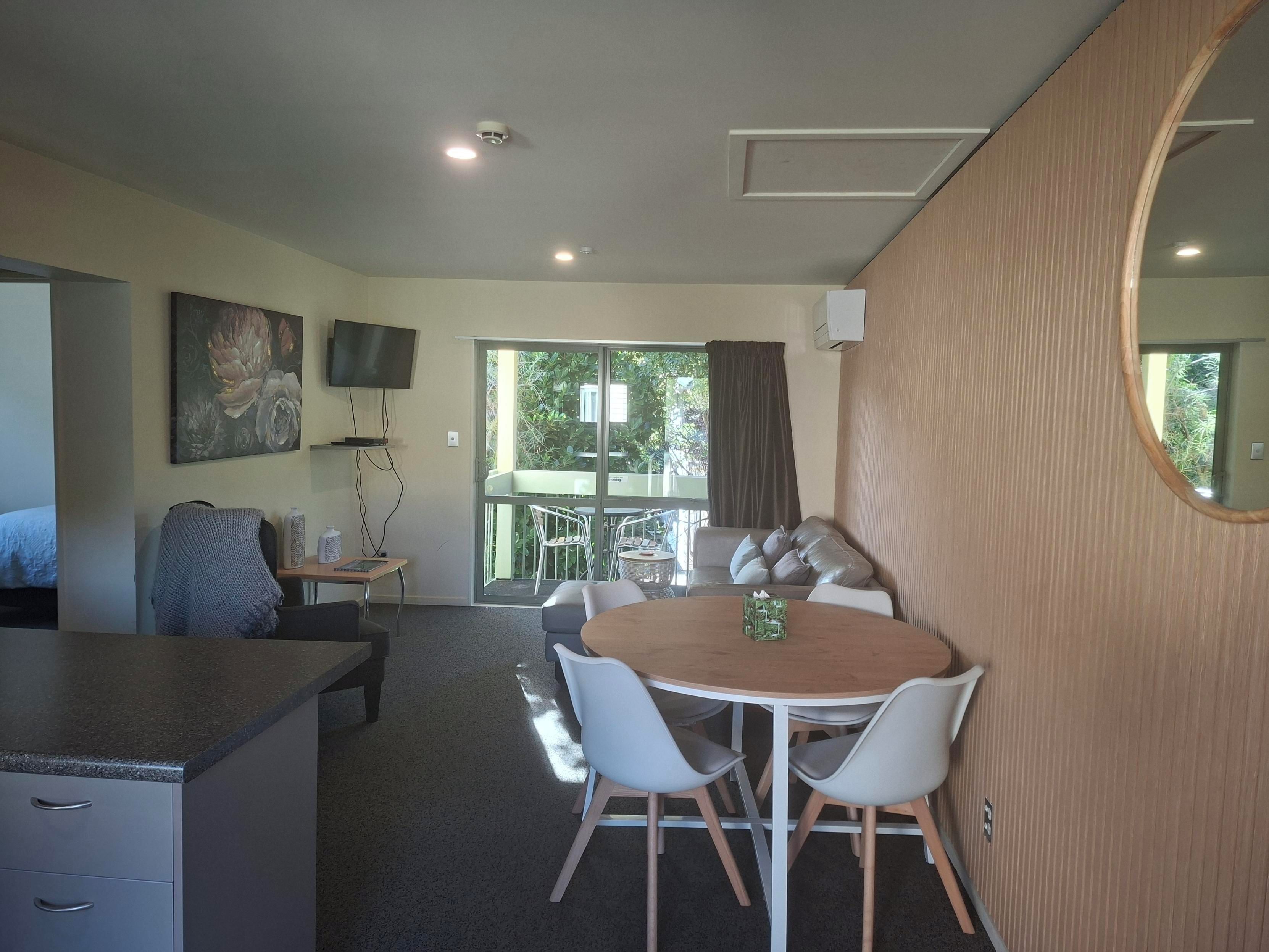 A modern room with a dining area, a television mounted on the wall, and a large mirror.