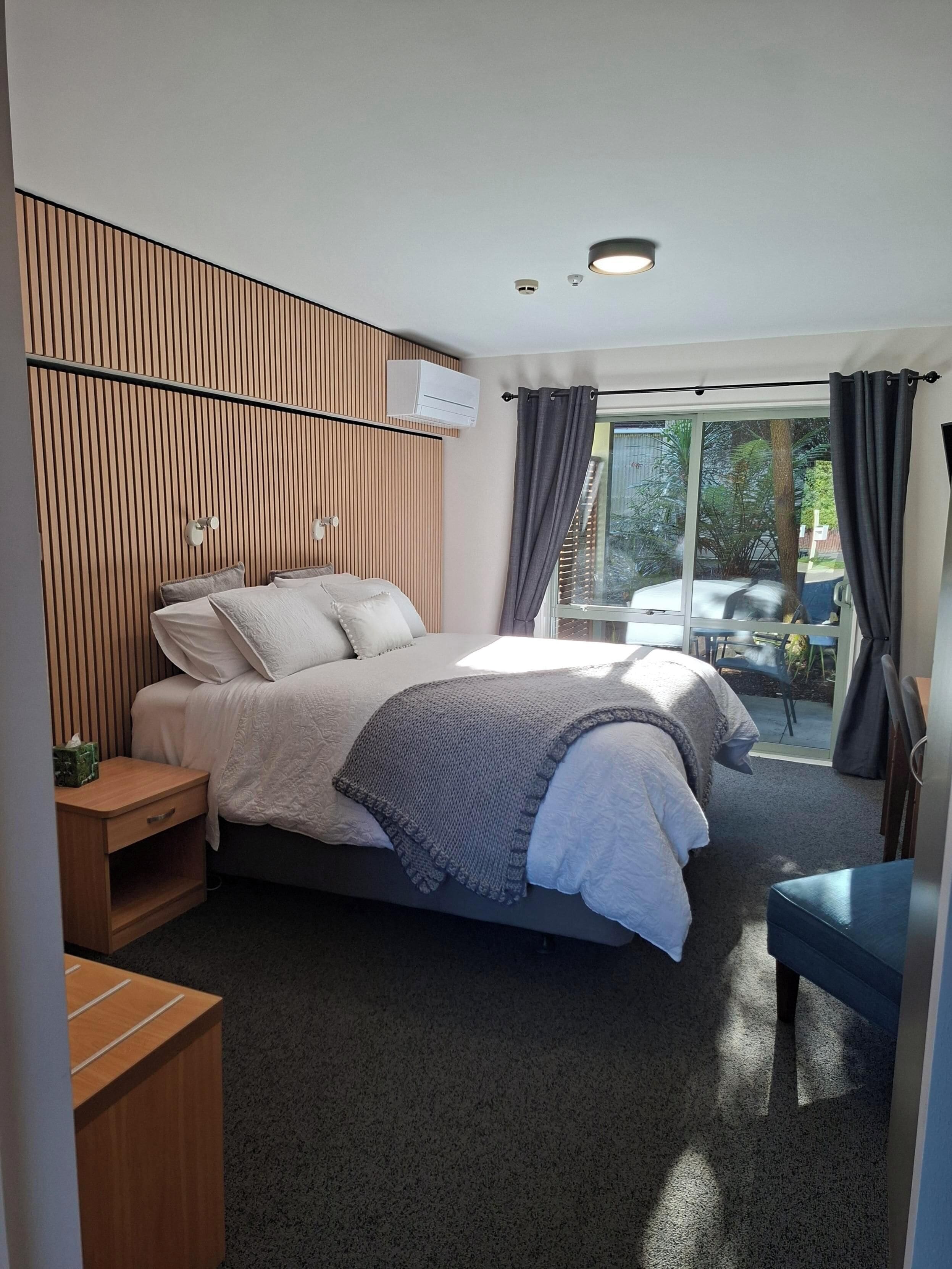 A modern bedroom with a bed, bedside tables, a desk, and a view of the outdoors.