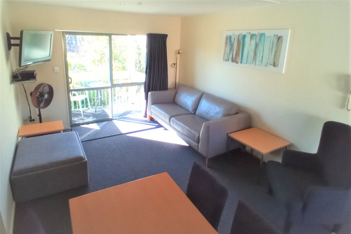 A living room with a sofa, two tables, a TV, and a sliding glass door to the outside.