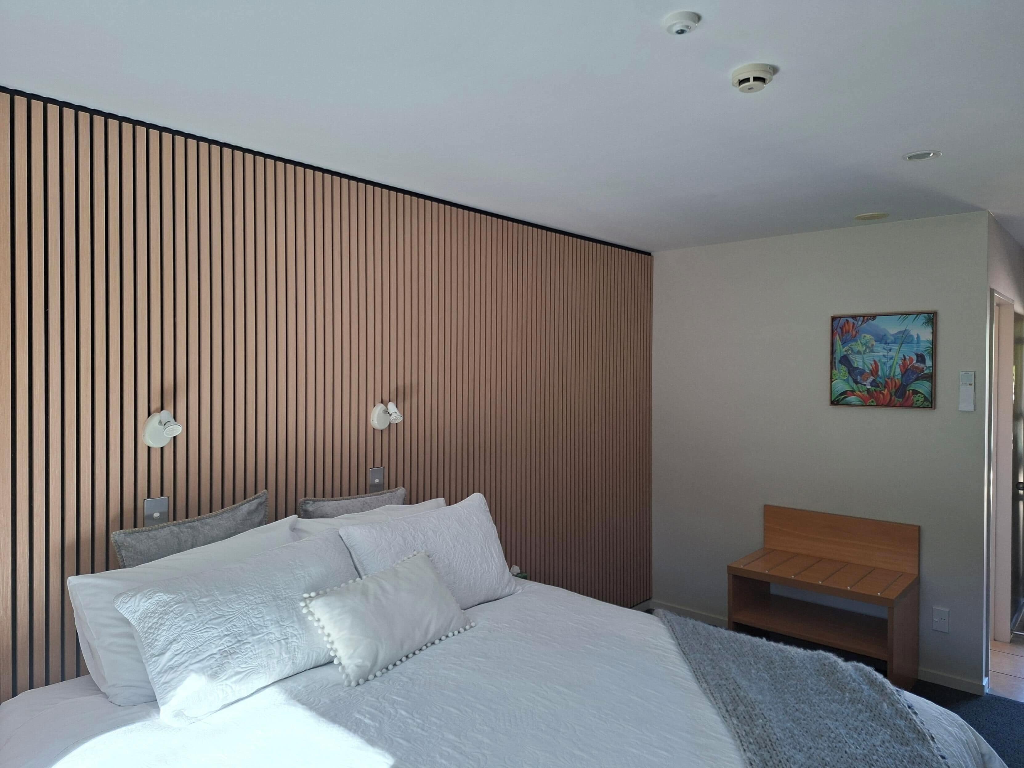A modern bedroom with a bed, bedside lamps, a wooden slat wall, and a painting on the wall.
