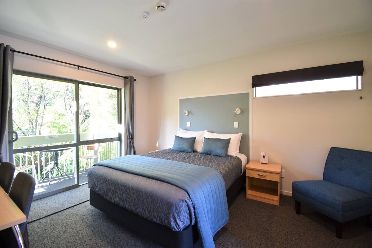 A bedroom with a large bed, a desk, a chair, and a window with curtains.