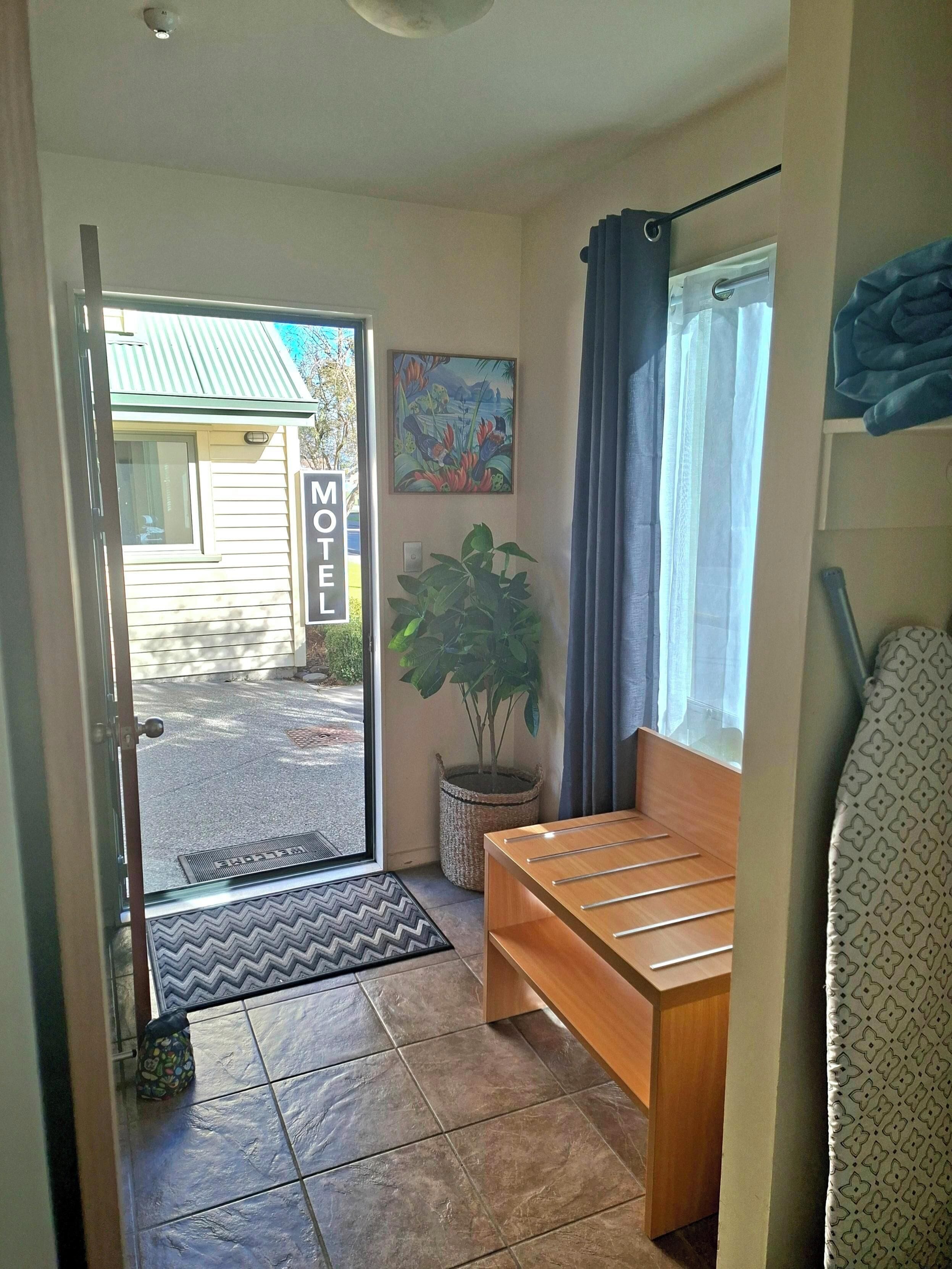 A motel room with a bench, a potted plant, a painting, and a view of the street.