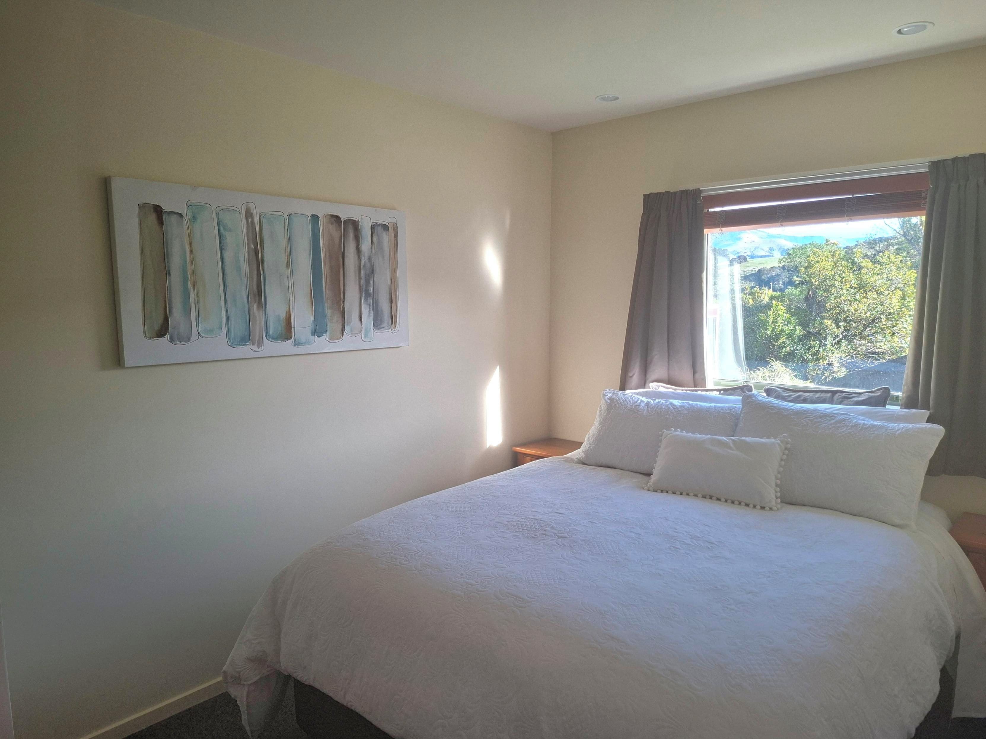A bedroom with a bed, a nightstand, a window with curtains, and a painting on the wall.