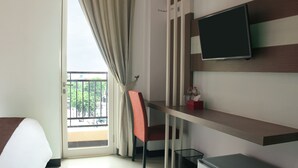 Quarto de hotel com uma cama, uma escrivaninha com cadeira, televisão na parede e varanda com vista para o verde.