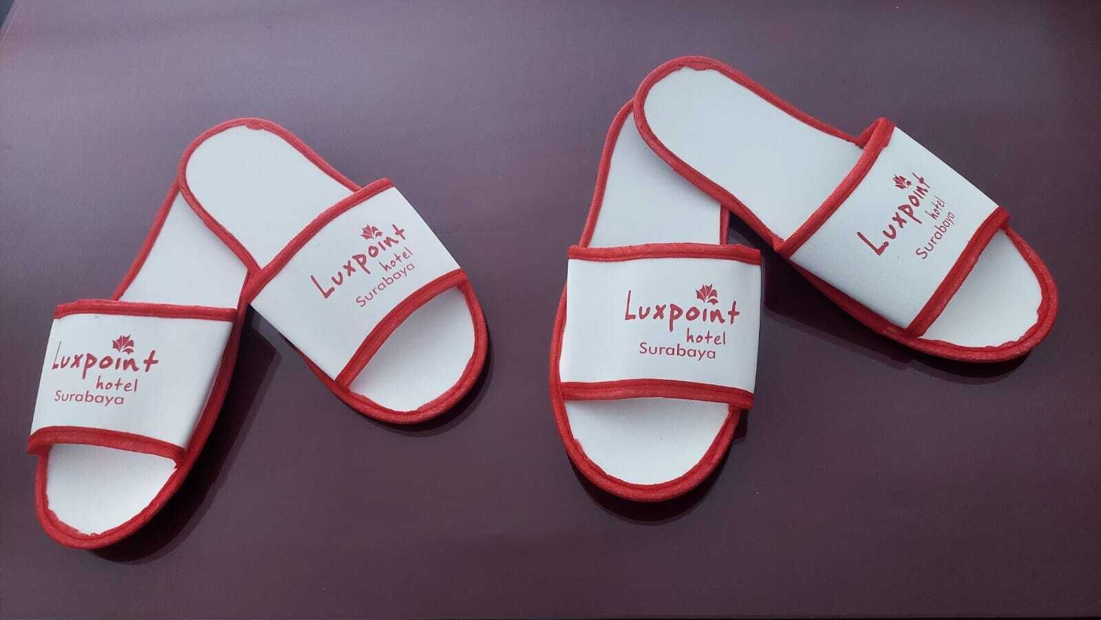 A pair of white and red slippers with the Luxpoint hotel Surabaya logo.