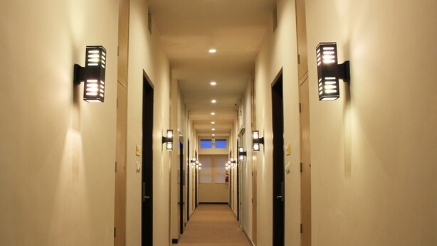 Corredor de hotel com várias portas, luminárias e piso coberto por carpete.