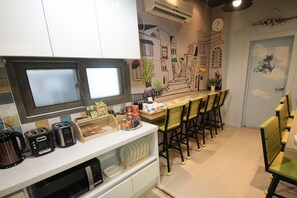 A kitchen with a microwave, toaster, and coffee maker. There are chairs and a table with a plant on it. - Soo Guesthouse (Seoul)