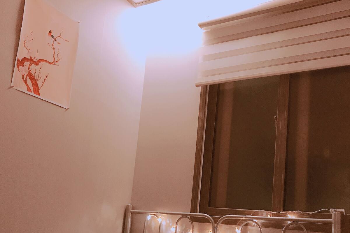 A bedroom with a bed, pillows, a window, and a wall-mounted artwork.