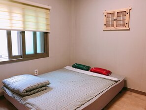 A small, single-bed room with a window, a wall-mounted calendar, and a bed with a checkered bedspread and pillows. - Soo Guesthouse (Seoul)