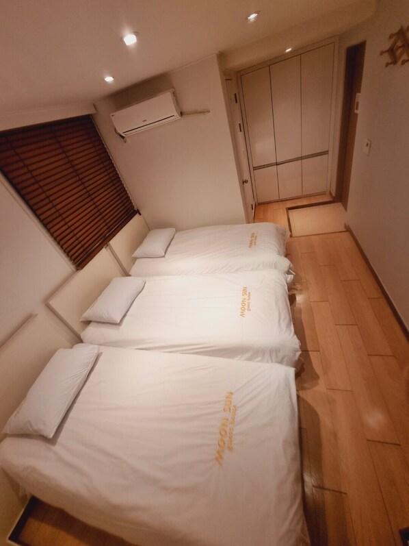 A hotel room with three single beds, a wardrobe, and an air conditioning unit. - Moon Sun Guesthouse (Seoul)