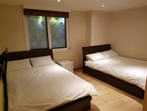 A hotel room with two single beds, a small bedside table, a window with frosted glass, and a wooden floor. - Moon Sun Guesthouse (Seoul)