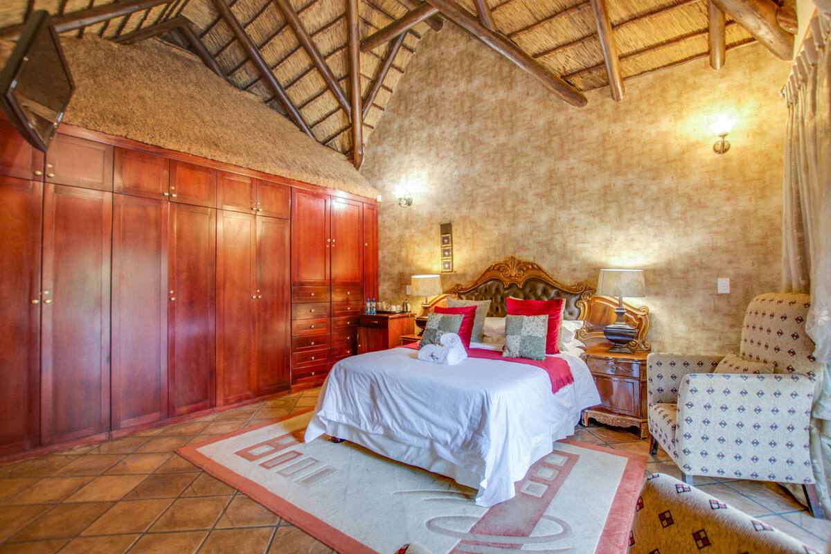 A bedroom with a large wooden wardrobe, a bed with white bedding, a nightstand with a lamp, and a patterned armchair.