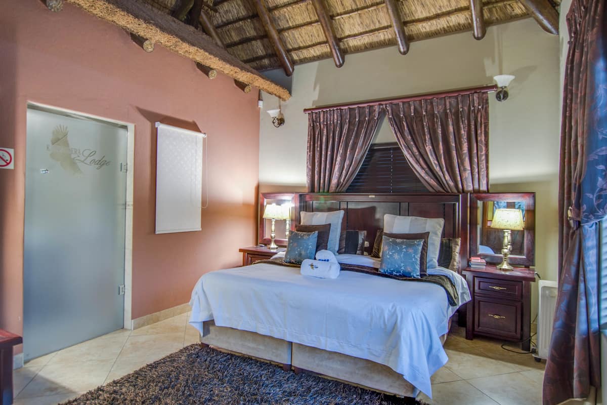 A bedroom with a large bed, two bedside tables with lamps, a wooden headboard, and a ceiling with exposed beams.
