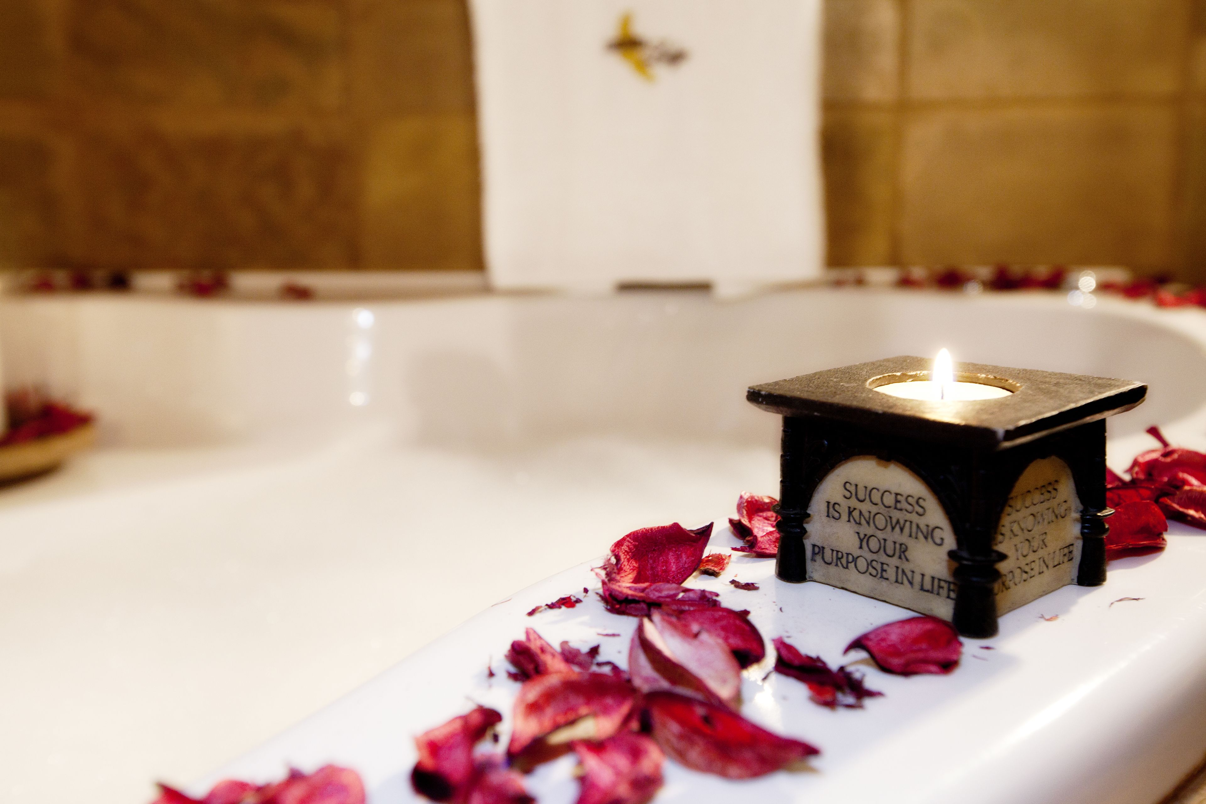 Ein Teelicht in einer Badewanne mit Rosenblättern und einer motivierenden Plakette.