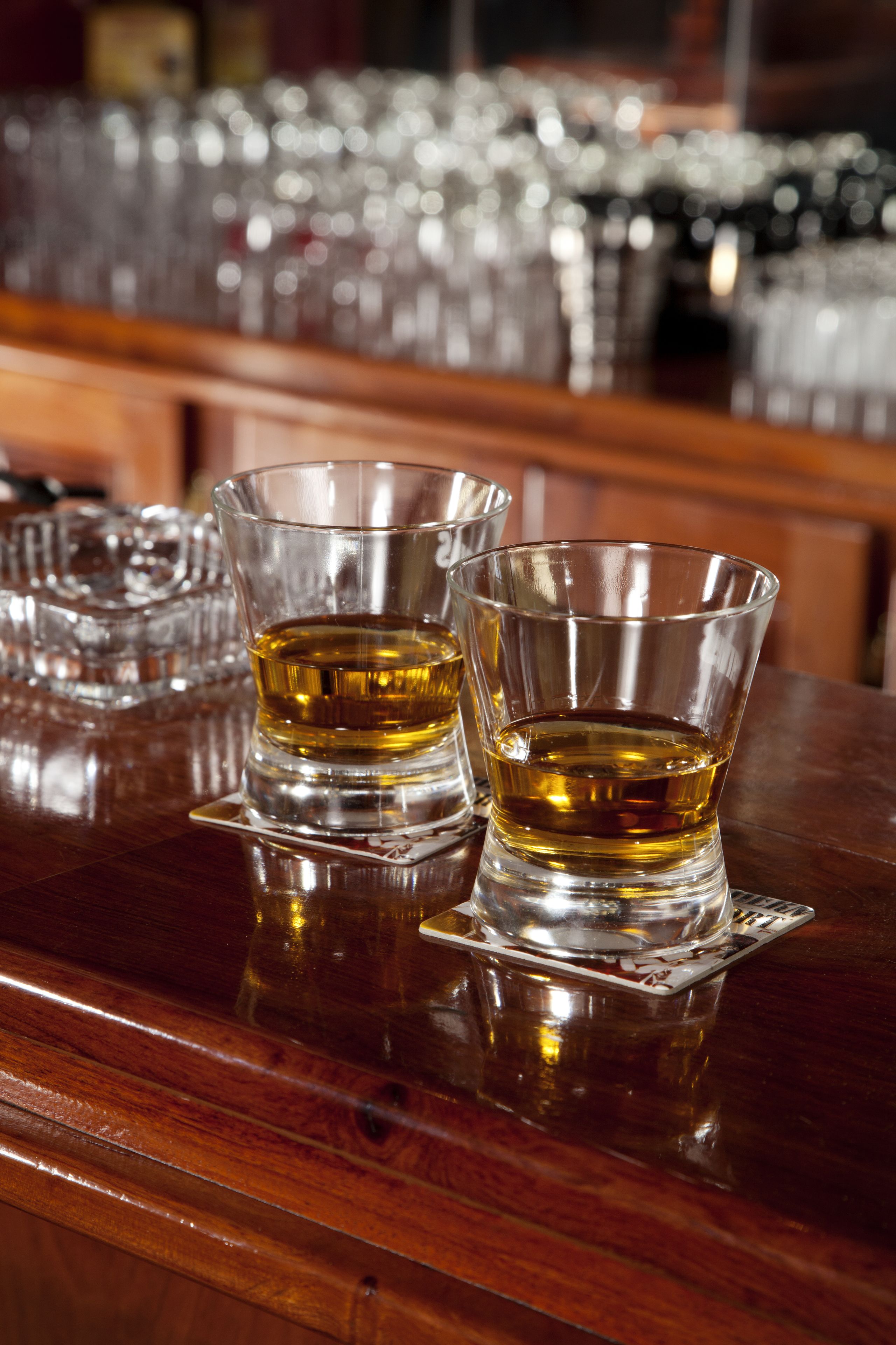 Two glasses of amber liquid on a reflective wooden bar counter.