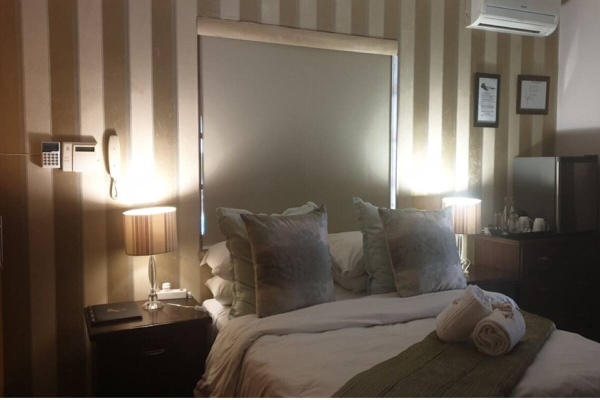 A hotel room with a bed, bedside lamps, a telephone, a mirror, and a refrigerator.