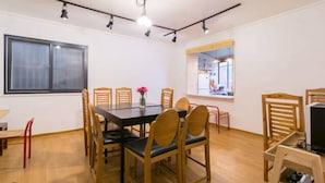 A dining area with a large table, wooden chairs, and a vase with flowers. - 9 Road - Hostel (Seoul)