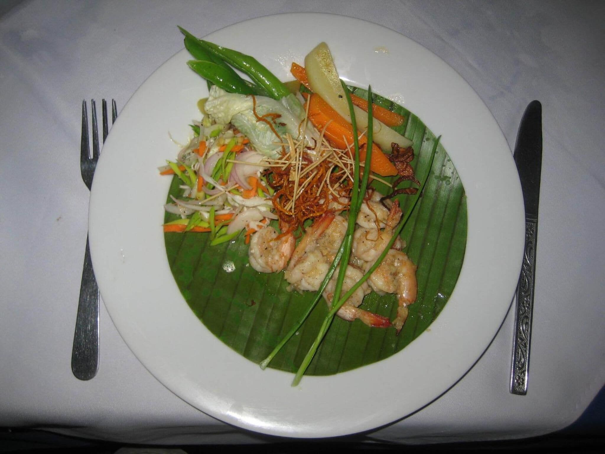 Un plato de comida sobre un mantel blanco, con un tenedor y un cuchillo a cada lado.