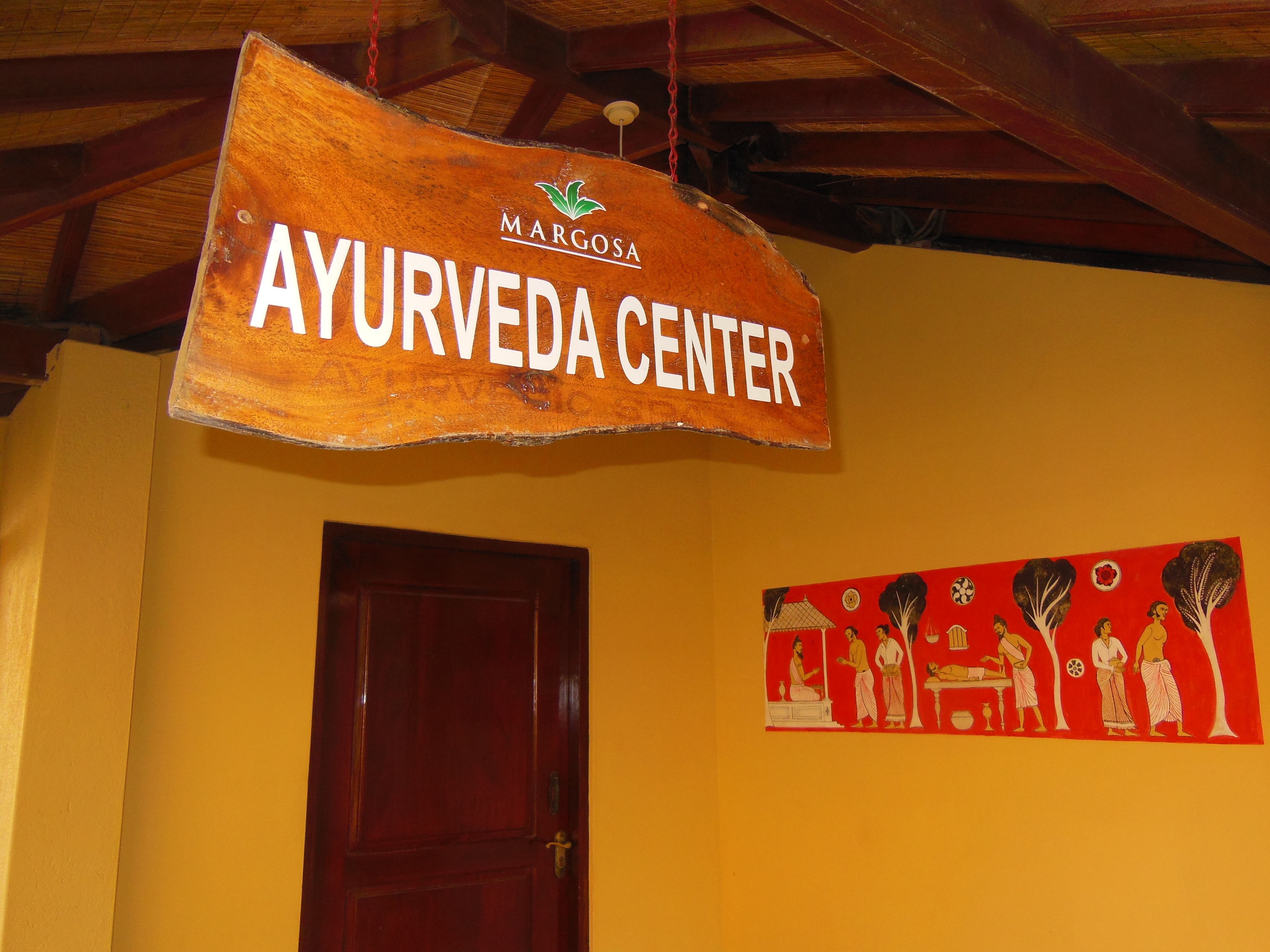 Ein hölzernes Schild mit der Aufschrift 'AYURVEDA CENTER', das über einer Tür hängt.