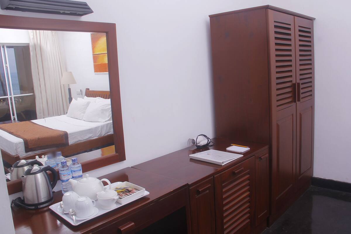Une chambre d’hôtel comprenant un lit, un bureau en bois avec un miroir, une armoire et un plateau avec des tasses à thé et une bouilloire.