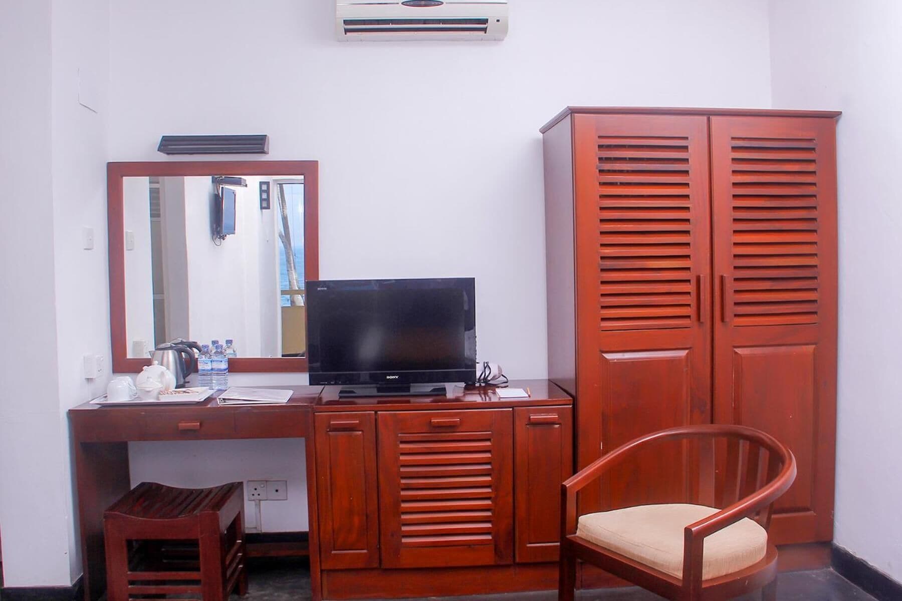 Una habitación con escritorio de madera, televisión, espejo, armario y una silla.